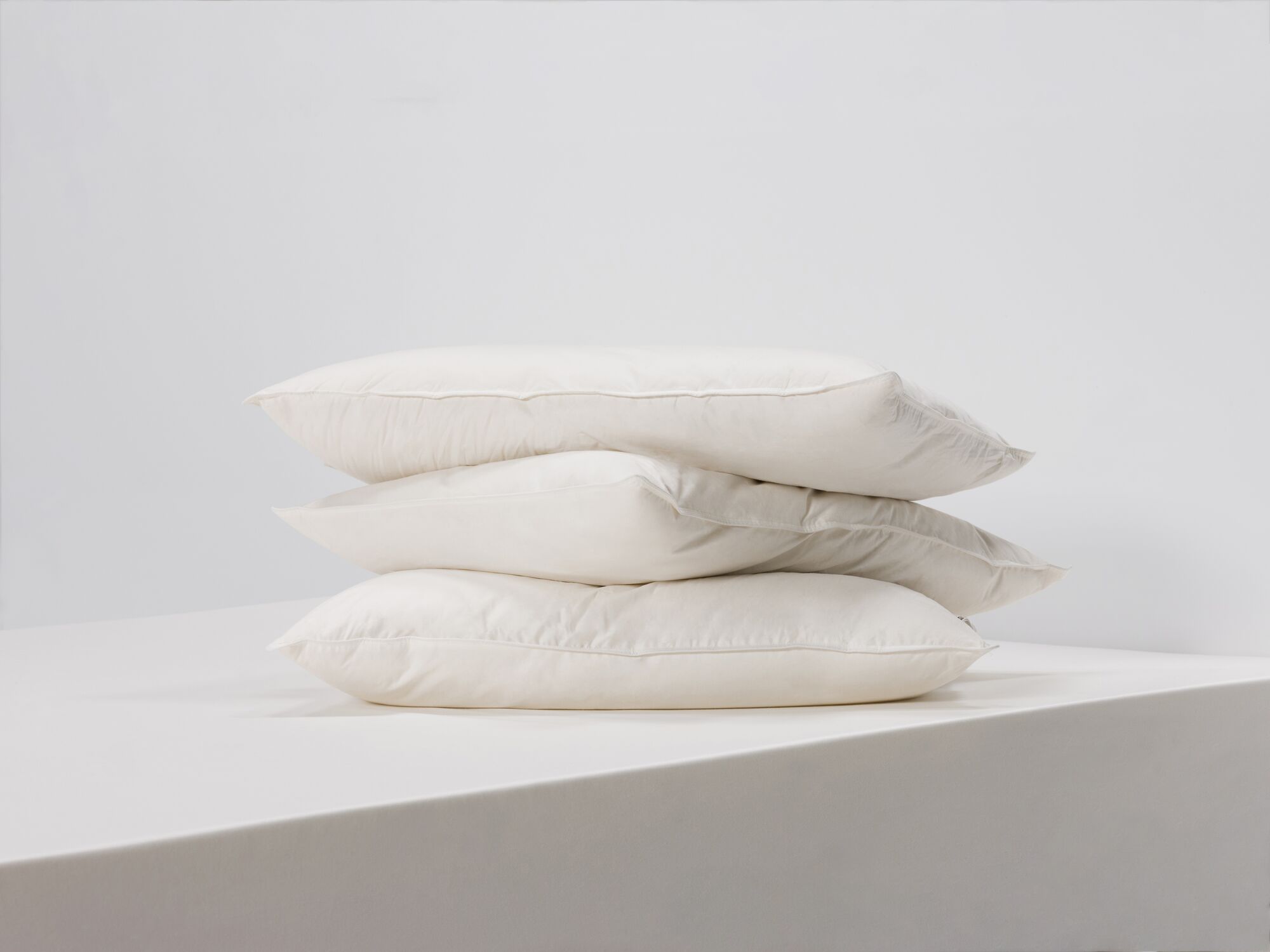 Side angle view of three queen size feather pillows stacked